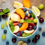 Bowl of healthy fresh fruit salad on a blue rusty background. Top view