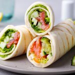 Wrap sandwich, roll with fish salmon and vegetables. Grey background. Close up.